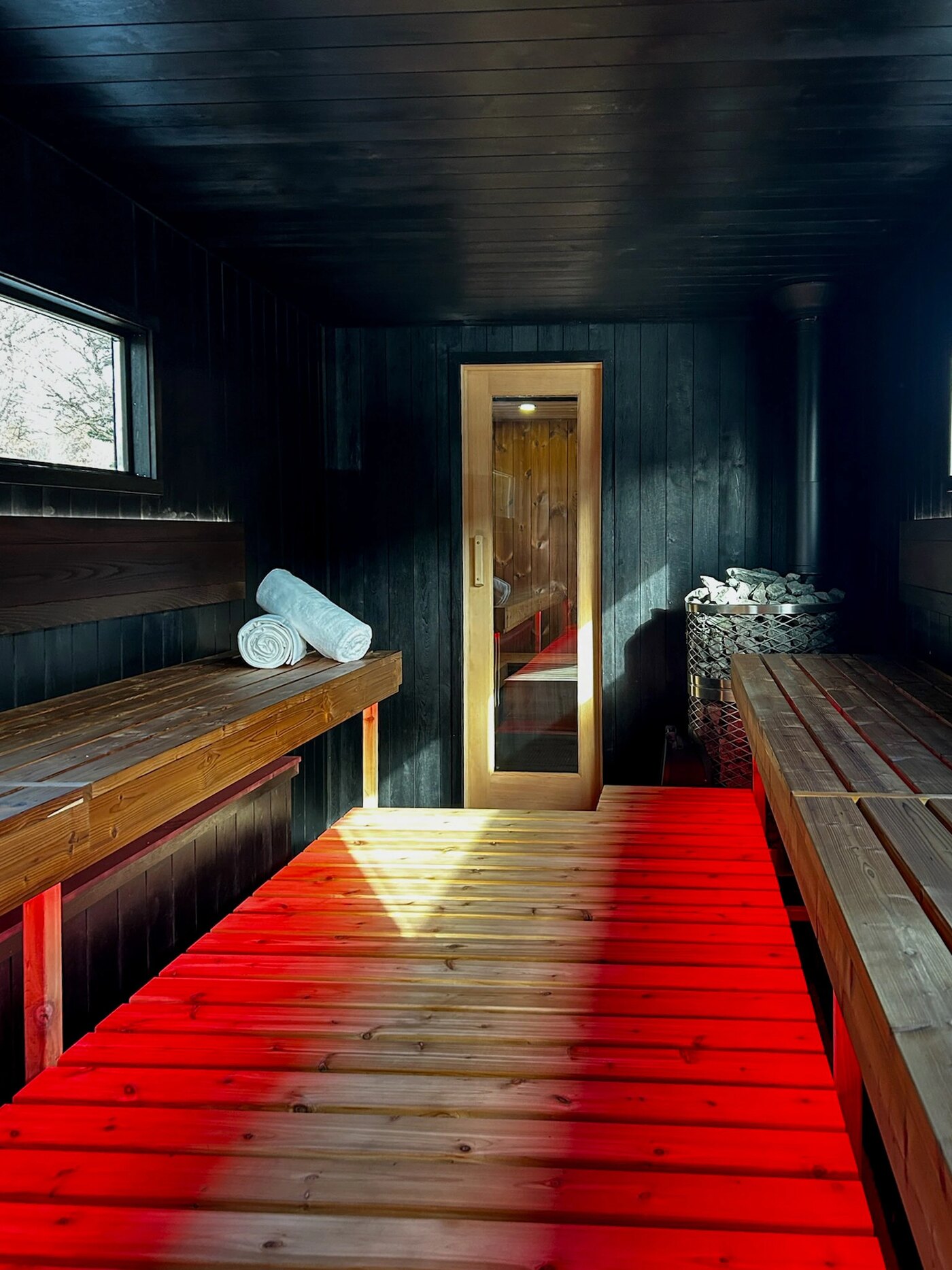 Dark sauna interior with folded towels and warm ambient light spilling through a glass door