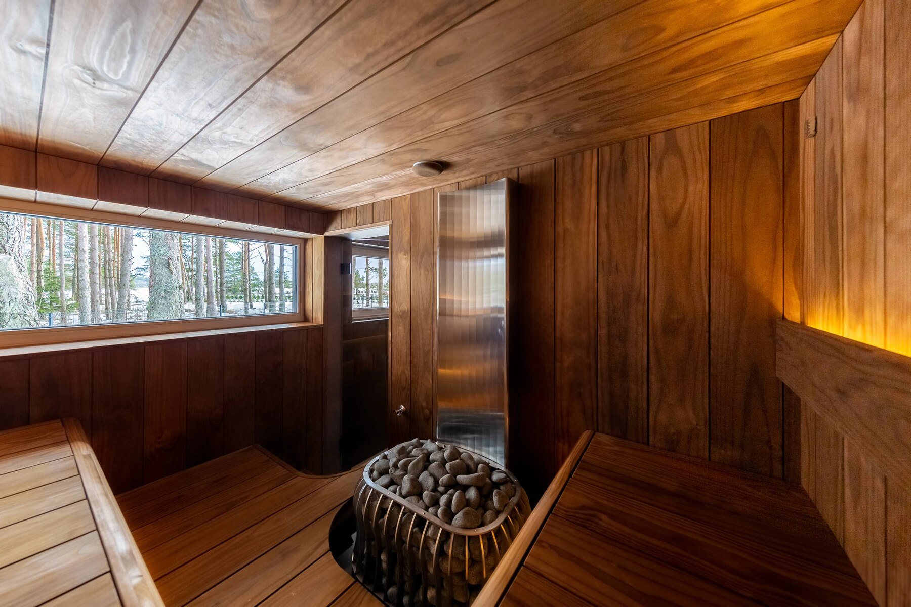 Custom sauna interior with warm wood paneling and a window looking out to snow-covered pines