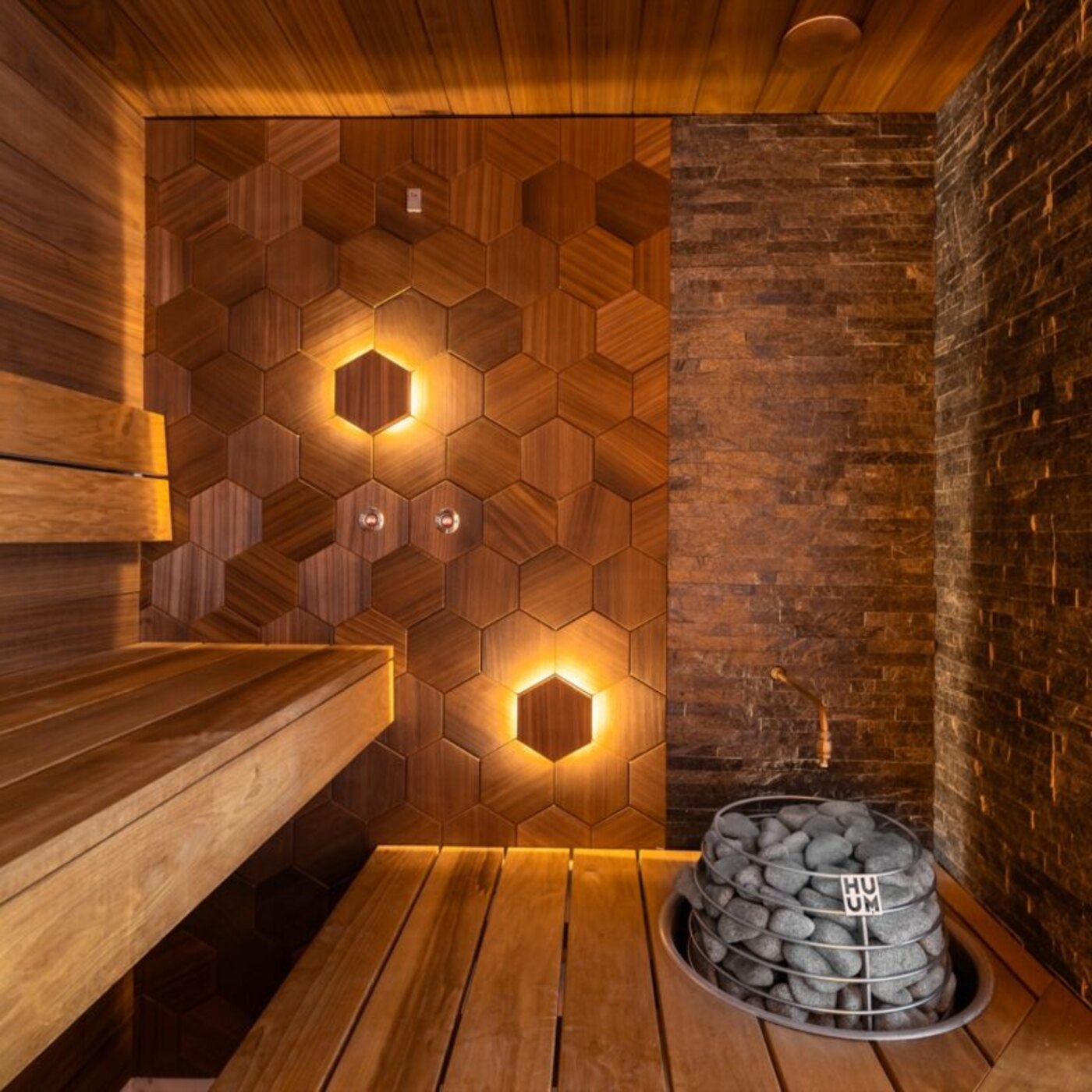 Luxury indoor sauna with backlit walnut hexagon paneling and a dark stacked-stone accent wall
