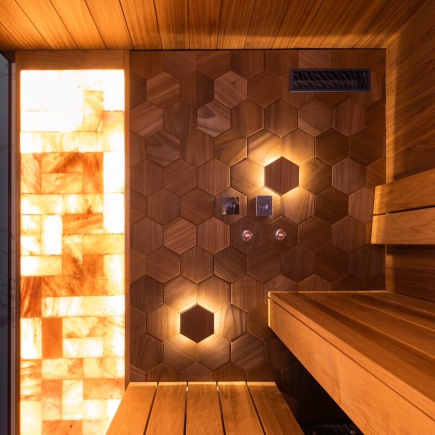 Wellness sauna suite with a glowing backlit salt wall beside hexagon wood paneling