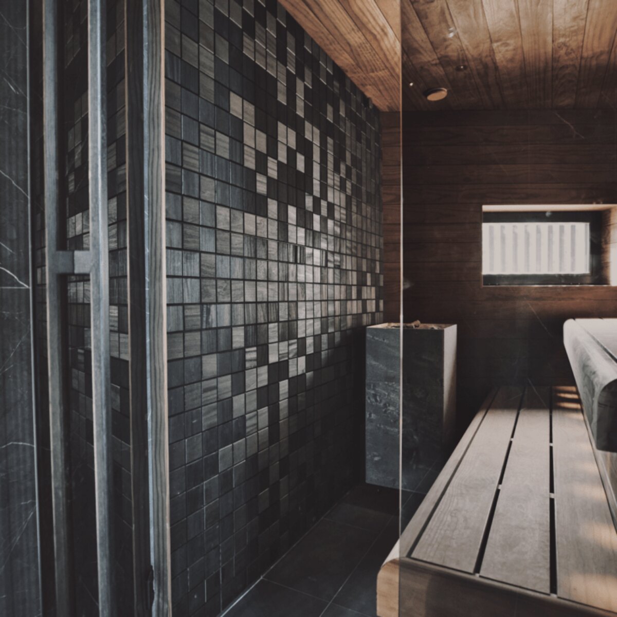 Sauna with a dark mosaic wood tile wall behind a glass partition